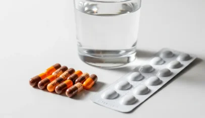 دواء إنتيتريكس كبسولات فموية موضوعة بجانب كوب ماء على سطح أبيض نظيف